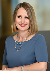 A smiling woman with shoulder length dark blond hair wearing a blue short sleeve shirt