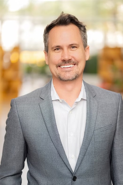 A smiling man with a grey suit and white shirt